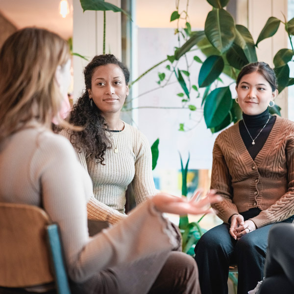 Woman sharing her experiences during a mental health group therapy meeting. Multiracial women participate in support group session sitting in a circle.