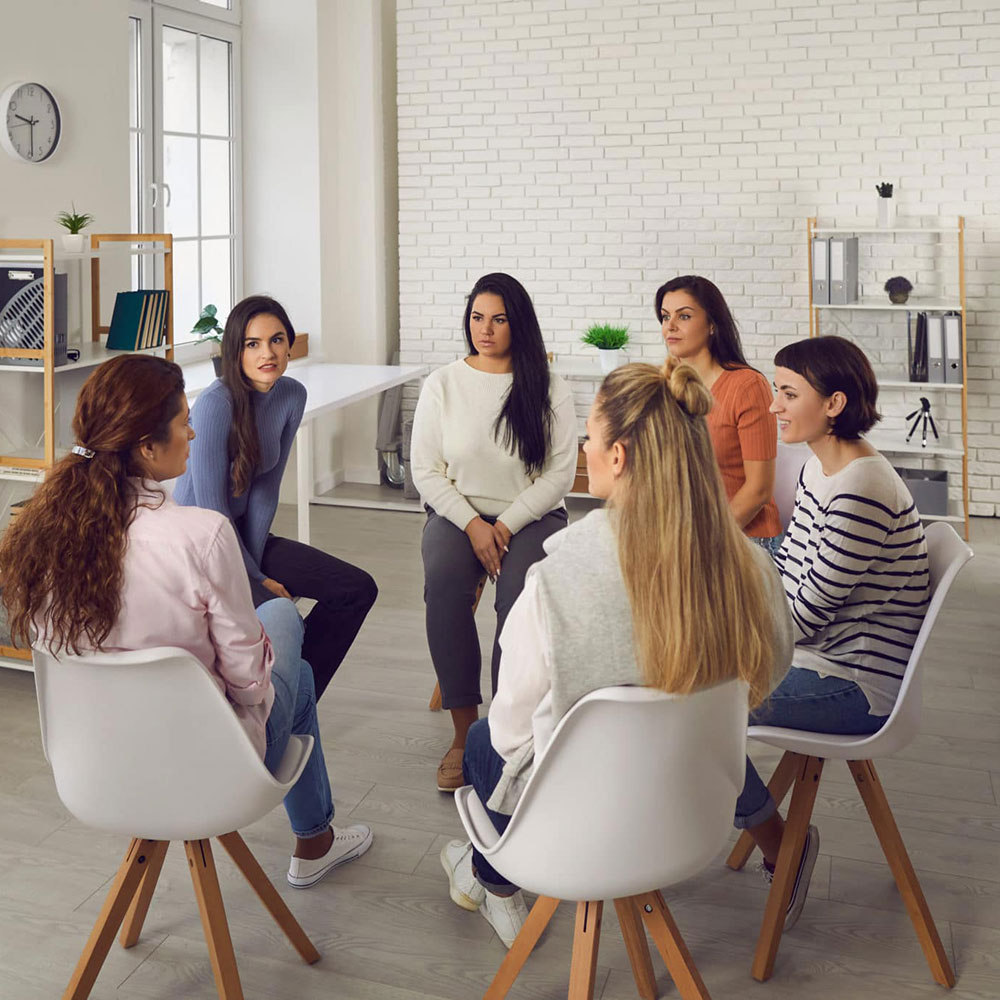 Young women telling their stories in therapy session or support group meeting. Female team talking, sharing news, discussing life situations, giving each other advice, working out solutions together.